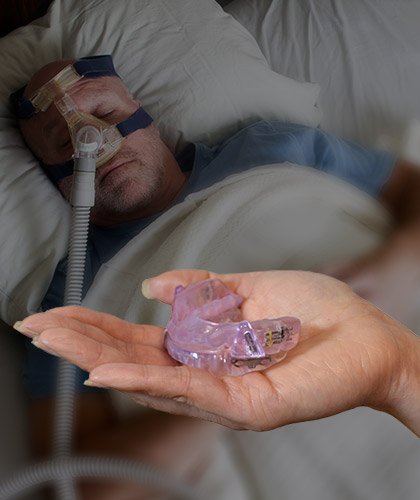 Man with a CPAP mask and hand holding an oral appliance